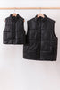 Two black puffer vests hanging on a rack against a white background